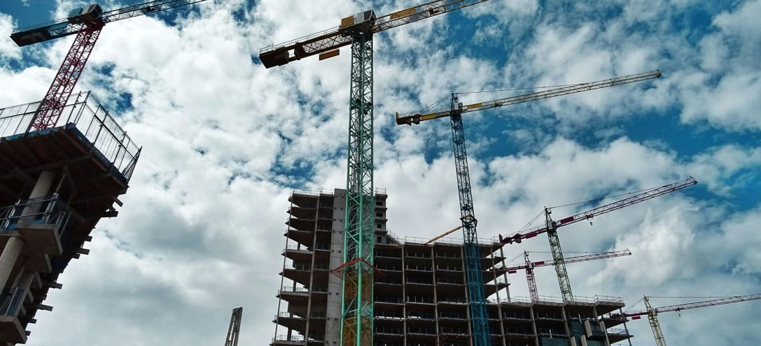 Urban construction site with numerous cranes framing rising skyscrapers against a blue sky.